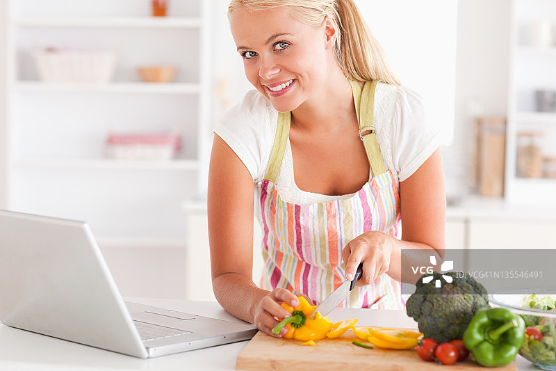 一个金发女人用笔记本电脑做饭的特写图片素材