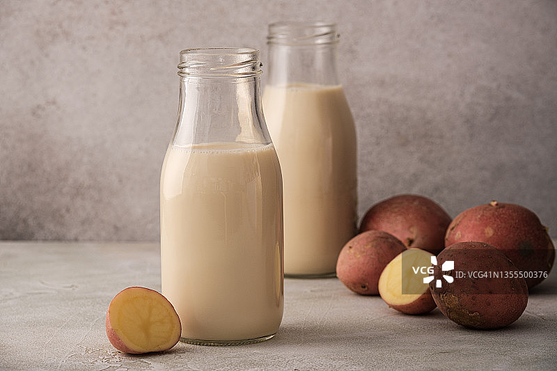 马铃薯牛奶替代非乳制品饮料在玻璃瓶上的灰色背景。健康素食和纯素饮料概念与复制空间图片素材