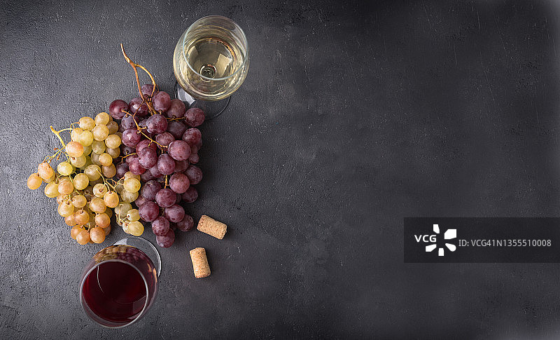 黑石桌上放着红、白葡萄酒和新鲜的葡萄。图片素材