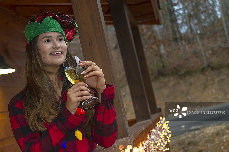 这是一个拉丁少女的肖像，在圣诞节的前几天，她在家外面感觉着美好的气味，喝着香槟，穿着冬季圣诞服装，在美国的森林中享受一个轻松寒冷的下午。图片素材