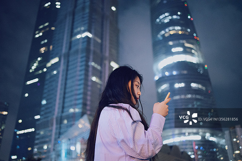 年轻的亚洲女商人在上海浦东著名地标使用智能手机图片素材