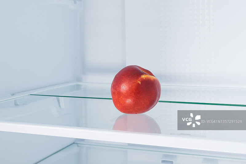 红油桃躺在空冰箱的架子上图片素材