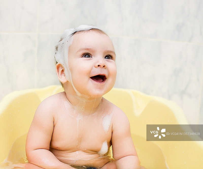 一个头发上有泡沫的漂亮宝宝正在洗澡。图片素材