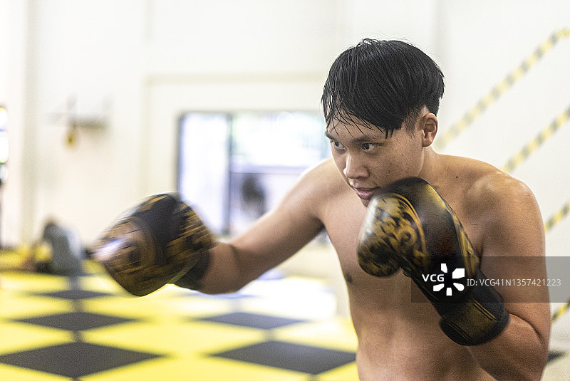 近面部表情亚洲年轻的成年拳击手练习拳击和拳击与黄色的拳击袋在拳击馆图片素材