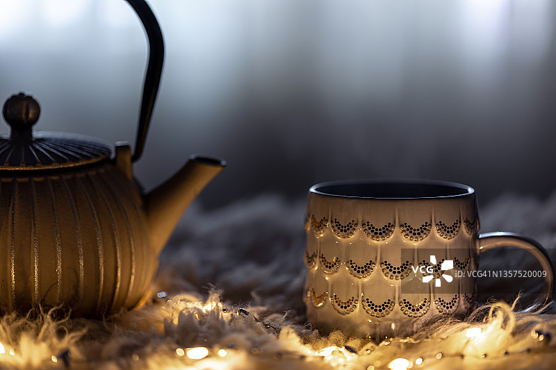 茶壶和杯子在黑暗中模糊的背景和花环。图片素材