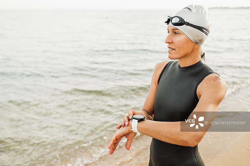职业铁人三项女运动员开始开放水游泳模式的智能手表和准备在海里游泳图片素材
