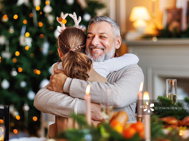 小女孩孙女抱着快乐微笑的爷爷在家里吃圣诞晚餐图片素材
