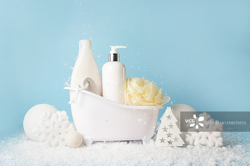 冬季护肤化妆品。白色空白瓶，乳液或保湿霜，洗发水和白色的雪粘贴蓝色的背景图片素材