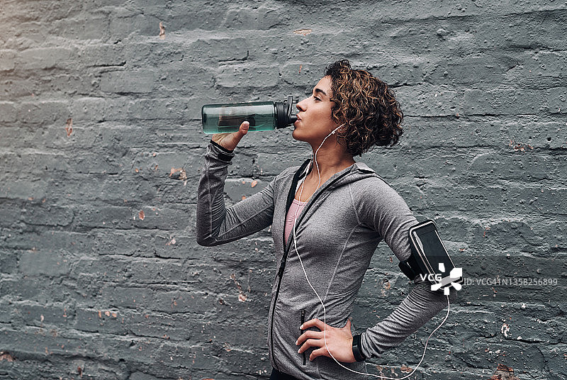 一个年轻女子在户外锻炼时喝水休息图片素材