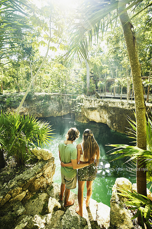 在丛林生态度假胜地放松时，拥抱的夫妇看着天然井的广角后视图图片素材