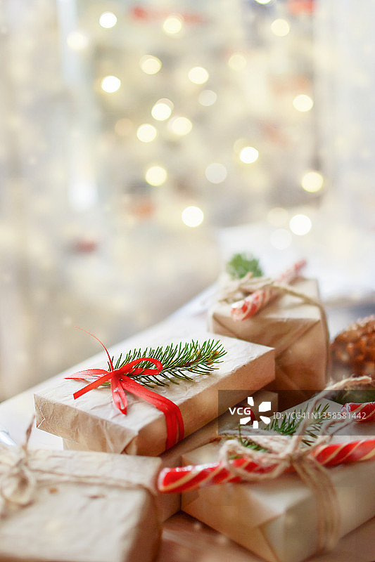 大量的礼品盒用工艺包装，用红丝带和黄麻线扎好，用红拐杖糖和云杉树枝装饰，映衬着模糊的圣诞彩灯，复制空间。图片素材