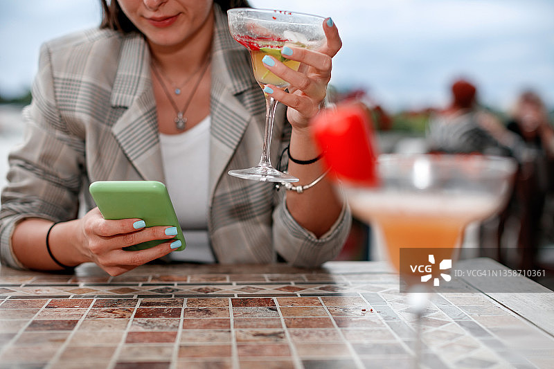 女人用智能手机发短信，在户外餐厅喝鸡尾酒图片素材