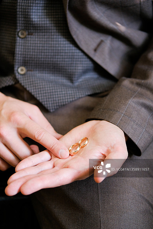 一个男人或新郎穿着昂贵美丽的豪华西装，在他的手掌上握着结婚金戒指，特写。婚礼，求婚，表白。图片素材