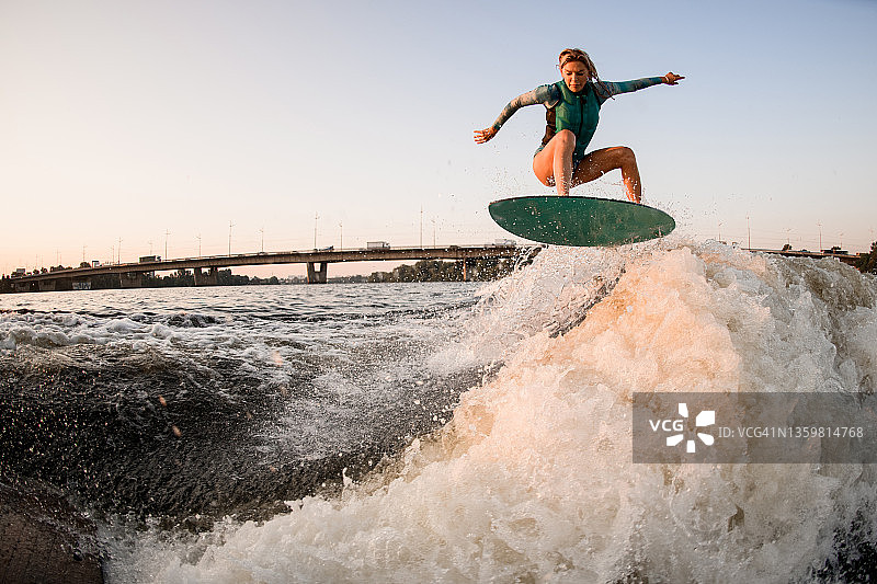 女子冲浪运动员熟练地跳上冲浪板，越过汹涌的河水波浪图片素材