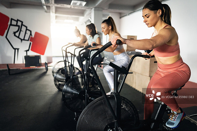 在现代健身房里，白人女运动员在固定自行车上锻炼图片素材
