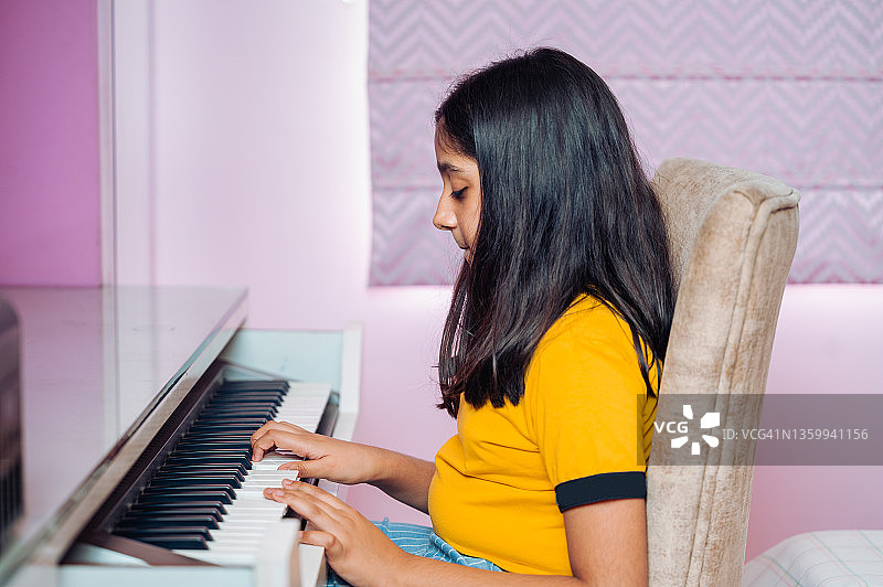 快乐的亚洲印度小女孩在家里客厅玩电子钢琴键盘。图片素材