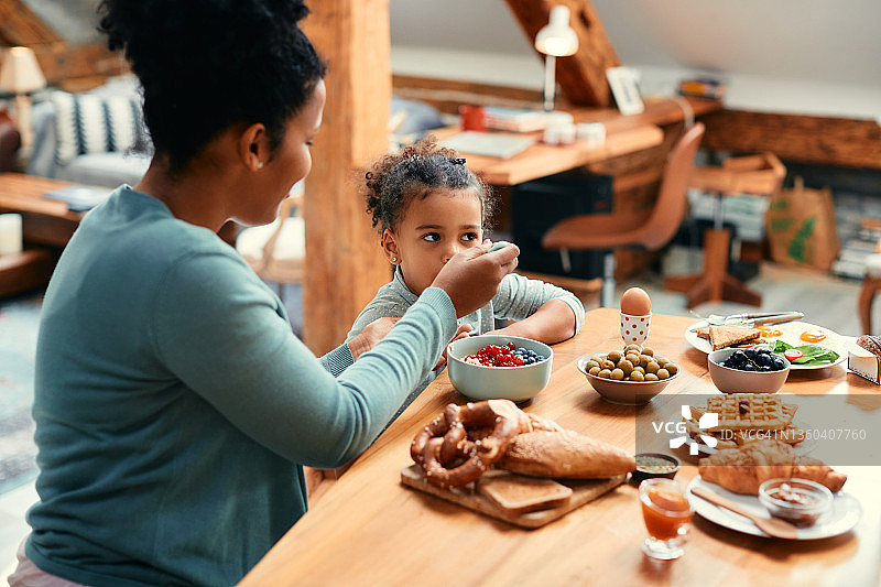 非洲裔美国母亲在餐桌上吃早餐时喂她的女儿。图片素材