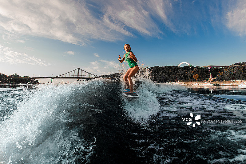 兴高采烈的女子在水上滑水板上积极地驾驭着河水的波浪，并摆出手势图片素材