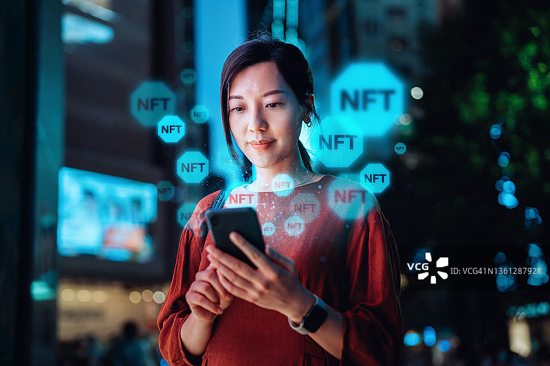 年轻的亚洲女性晚上在市中心街道使用智能手机，使用区块链技术工作，投资或交易加密货币、数字资产、艺术品和数字账簿图片素材
