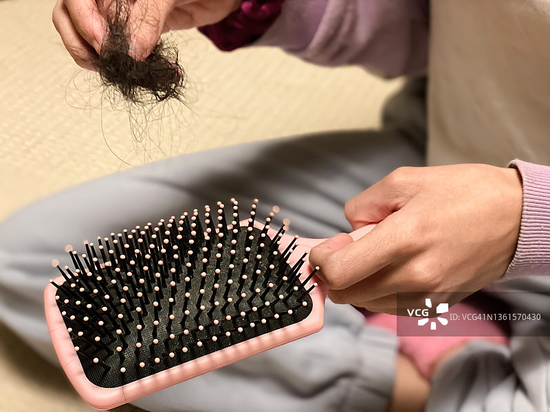 一名混血年轻女性梳完头发后从梳子上抽出一缕缕头发图片素材