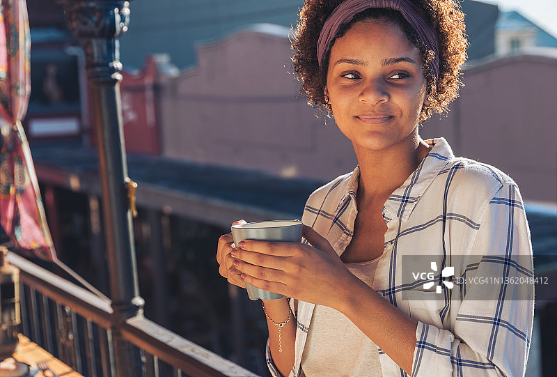 微笑的年轻女子在阳光明媚的阳台上喝咖啡图片素材