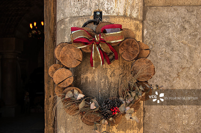 乡村圣诞花环装饰，由木片，干草和树枝，松果和丝带，挂在建筑物的外部图片素材