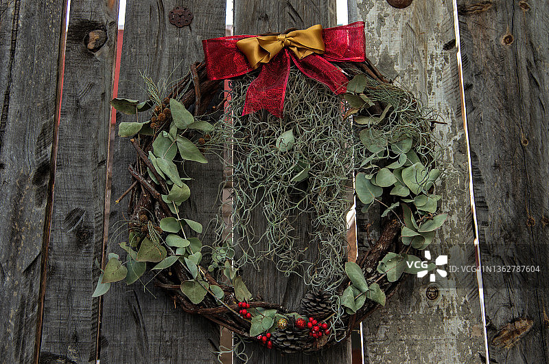 古色古香的圣诞花环，用树枝、苔藓、松果和丝带做成，挂在饱经风霜的木栅栏上图片素材