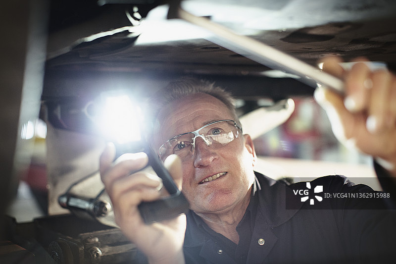 男性机械师，在汽车修理店工作，在车底下使用手电筒图片素材