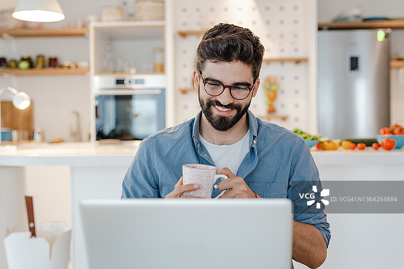 一个年轻人在家里一边喝咖啡一边用笔记本电脑工作图片素材