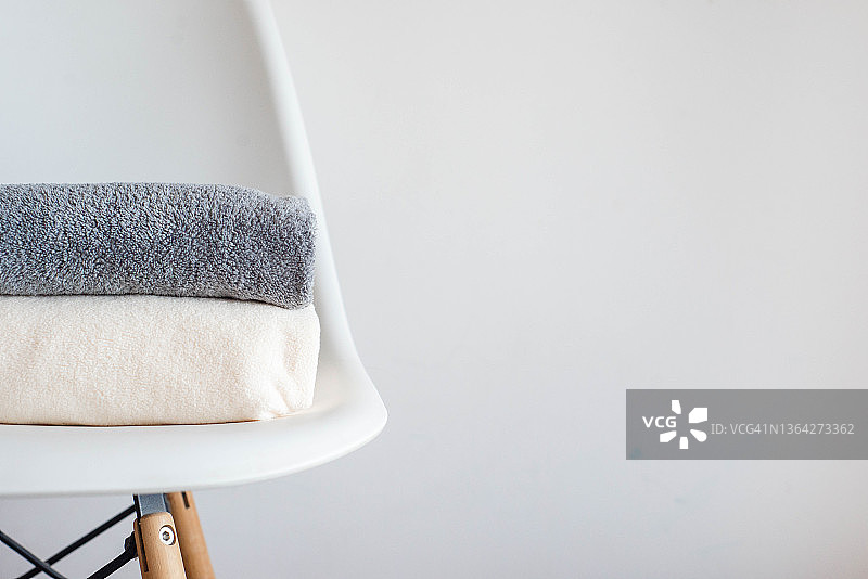 在白色的背景下，毛巾和柔软的羊毛布整齐地叠在椅子上。干净的房子，有序的房子，简约主义。图片素材