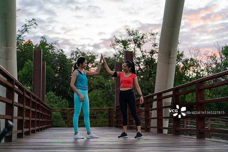 亚洲女性早上在公园里击掌，享受慢跑的乐趣。图片素材