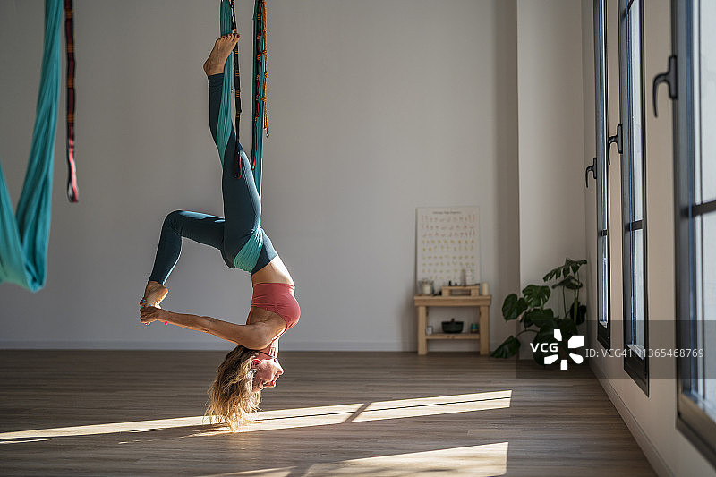 健身俱乐部，一名女子倒挂在空中丝绸上练习瑜伽图片素材