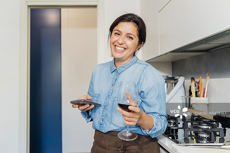 家里厨房里拿着酒杯拿着智能手机的快乐女人图片素材