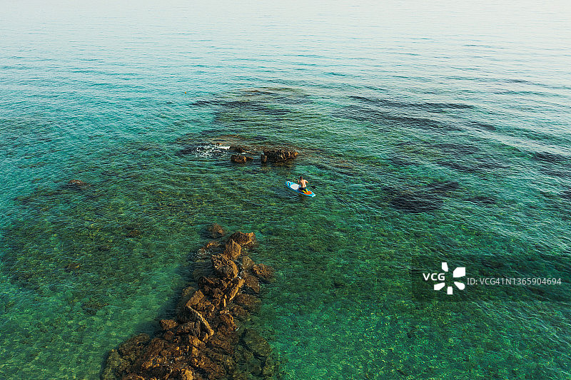 希腊扎金索斯岛，男子在碧绿的海面上用桨冲浪的鸟瞰图图片素材