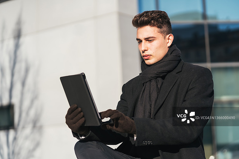 冬天，时尚的年轻白人商人在办公室外，戴着手套，用平板电脑阅读电子邮件图片素材