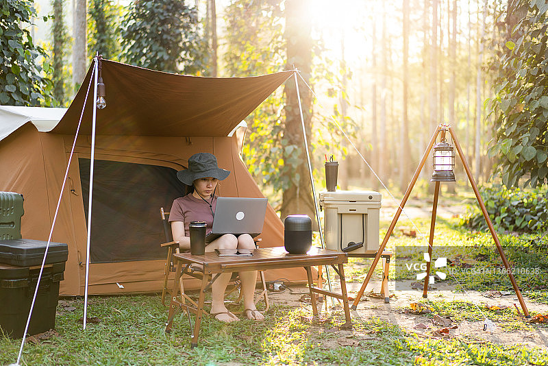 周末度假露营时，一个女人坐在帐篷前，用笔记本电脑远程工作图片素材