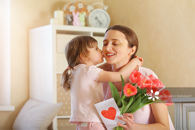 母亲节快乐。女儿祝贺她的母亲，并给她一个自制的卡片和粉红色的郁金香图片素材