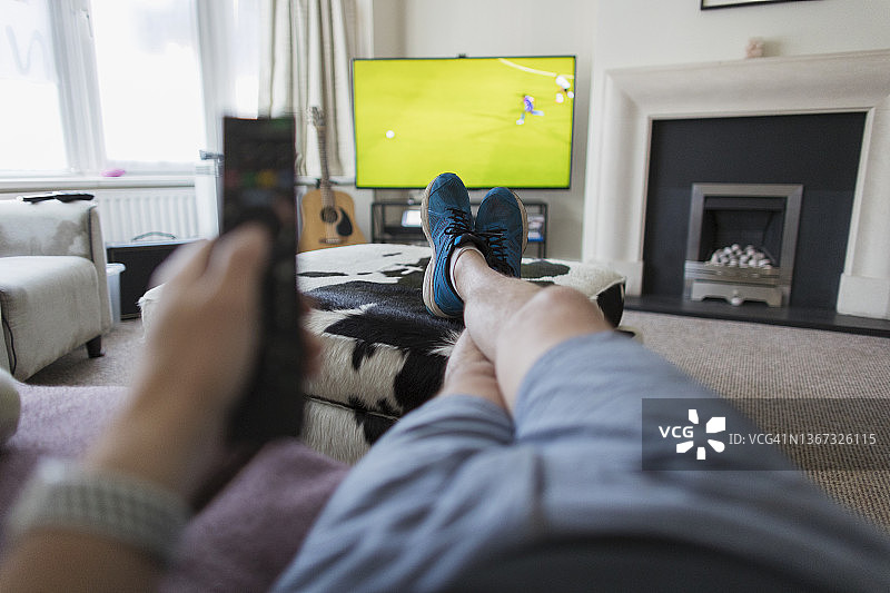 POV人坐在沙发上拿着遥控器看电视上的足球比赛图片素材
