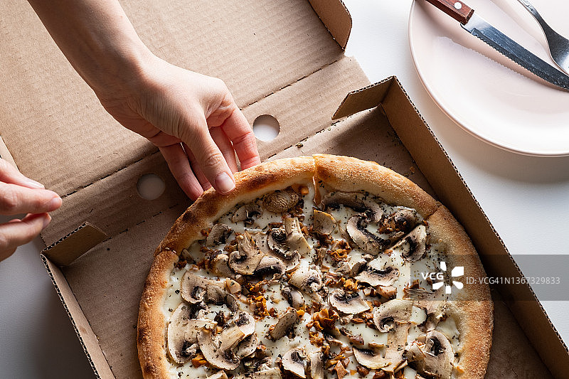 意大利蔬菜披萨切片，有奶酪、蘑菇和香槟，装在纸盒或包装里，可以在家里、咖啡馆或披萨店送餐。一个女人拿了一块披萨吃了。素食理念，送货上门。快餐图片素材