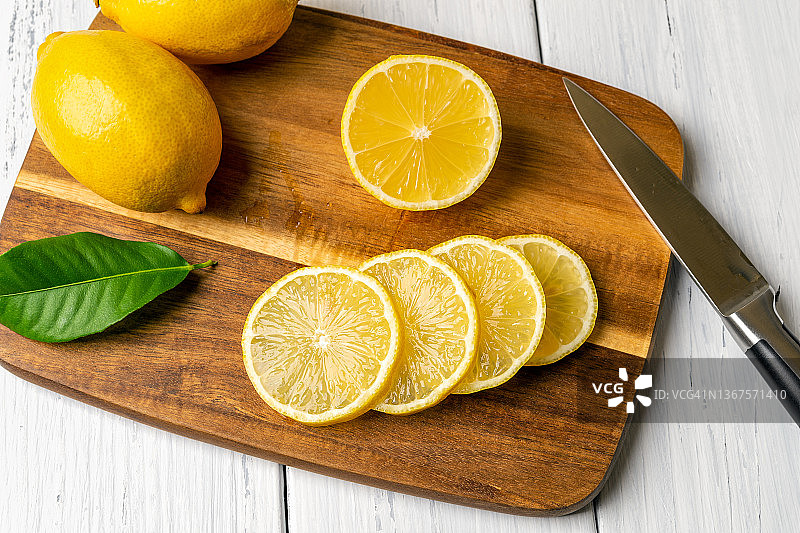 整个柠檬和多汁的切片放在棕色的木制砧板上。用刀切柑橘。生柠檬具有维生素C、抗氧化、烹饪和健康饮食的理念。酸味水果。图片素材