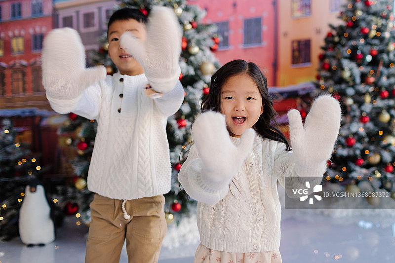 亚洲小男孩和小女孩站在溜冰场上向镜头展示手套图片素材
