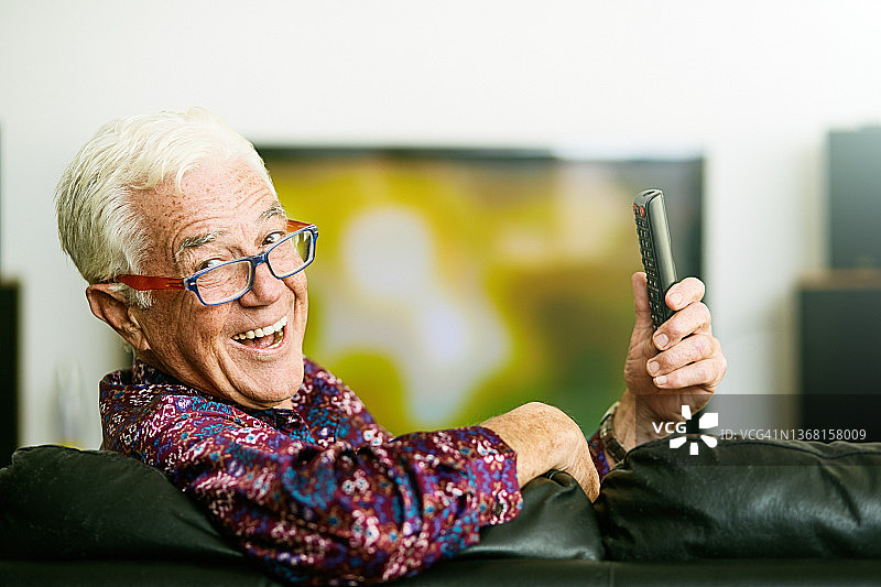 坐着的老人一边拿着遥控器看电视，一边开心地笑着图片素材