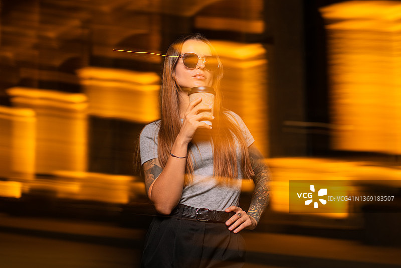 动态模糊肖像的现代年轻女子戴着太阳镜，拿着一杯咖啡图片素材