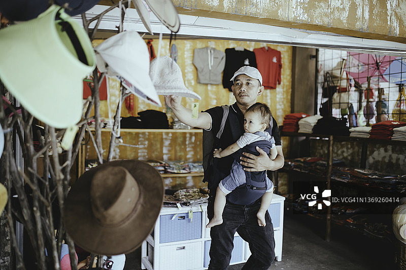 一名亚洲男子抱着孩子向店主展示服装选择图片素材