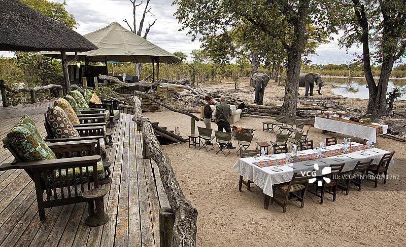日落时分，游客们坐在狩猎旅社前的水坑里观看大象饮水图片素材