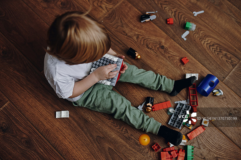 一个美丽的微笑的男孩坐在木地板和玩彩色立方体的肖像图片素材