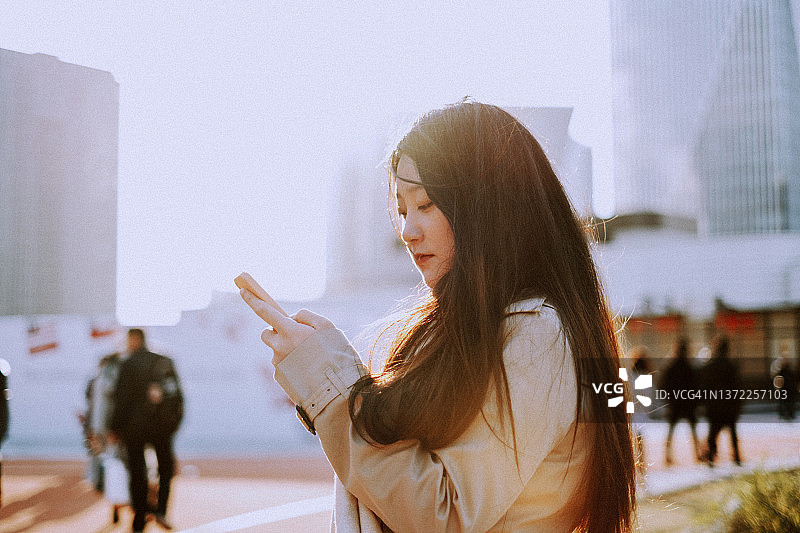 年轻的亚洲女性在晨曦中手持智能手机图片素材