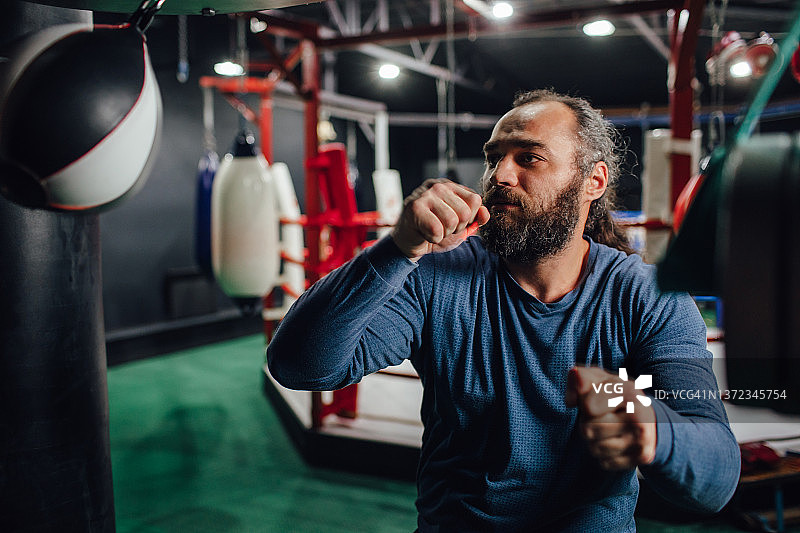 一名留着长发的亚美尼亚男子在拳击台的背景下击打出拳袋图片素材