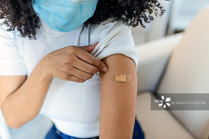 一名非洲妇女在接种疫苗后，举起她的衬衫袖子，露出包扎着绷带的手臂。covid 19免疫图片素材