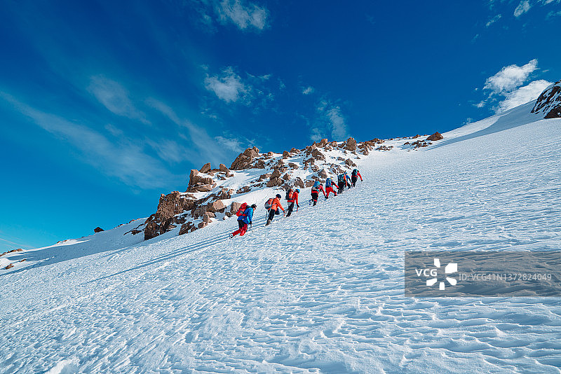高山登山队在冬季在高海拔山峰上排成一行行走图片素材
